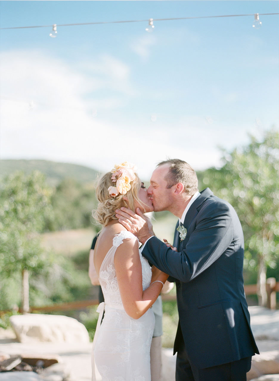 A bride with a flower crown and groom share a kiss together in an outside ceremony at their Ranch wedding in Utah.
