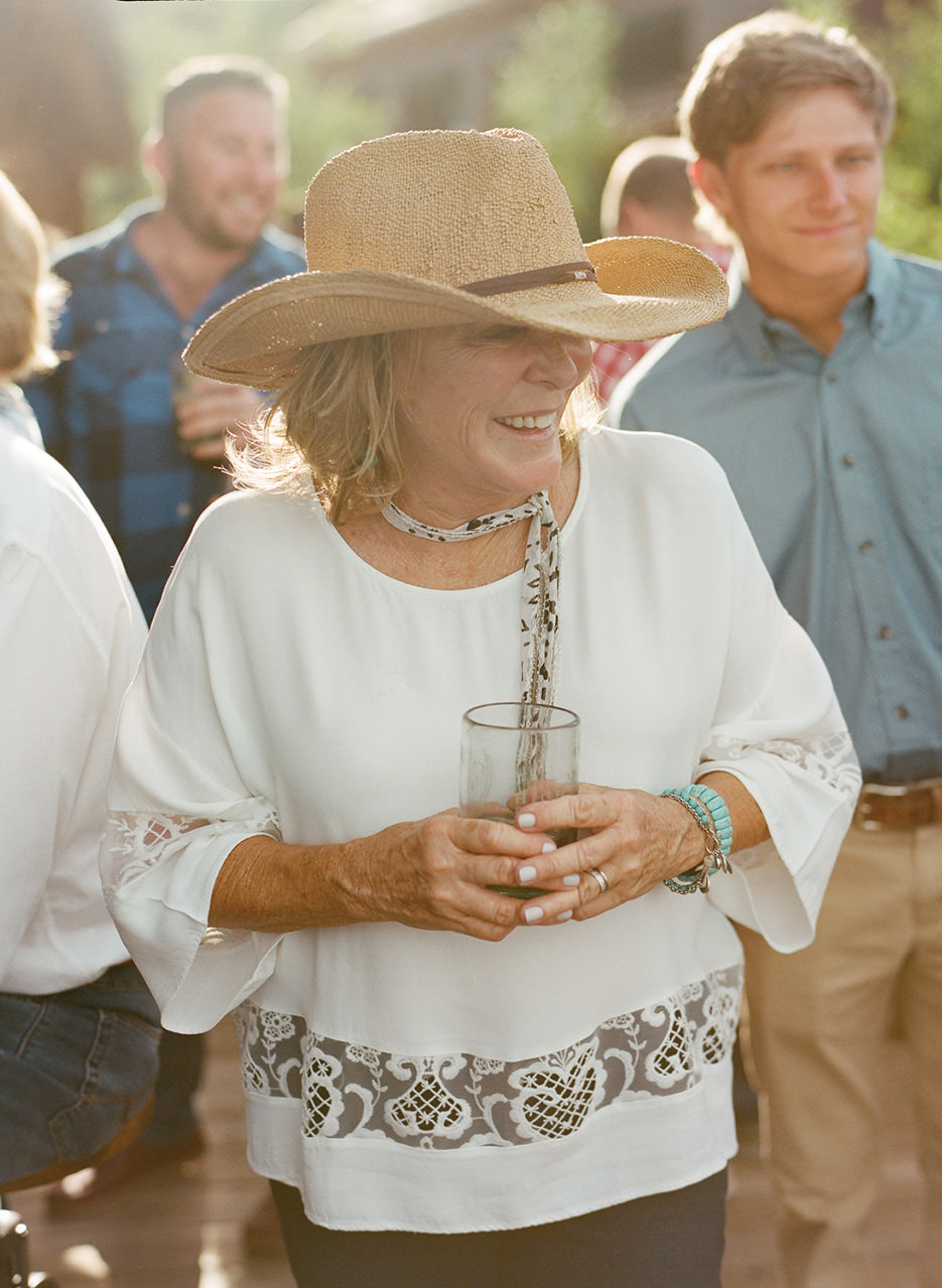A woman in a cowboy hat and western attire smiles with a drink in hand