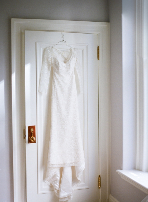 A long sleeve lace bridal gown hangs from a white doorframe in the Palace Hotel in San Francisco. 