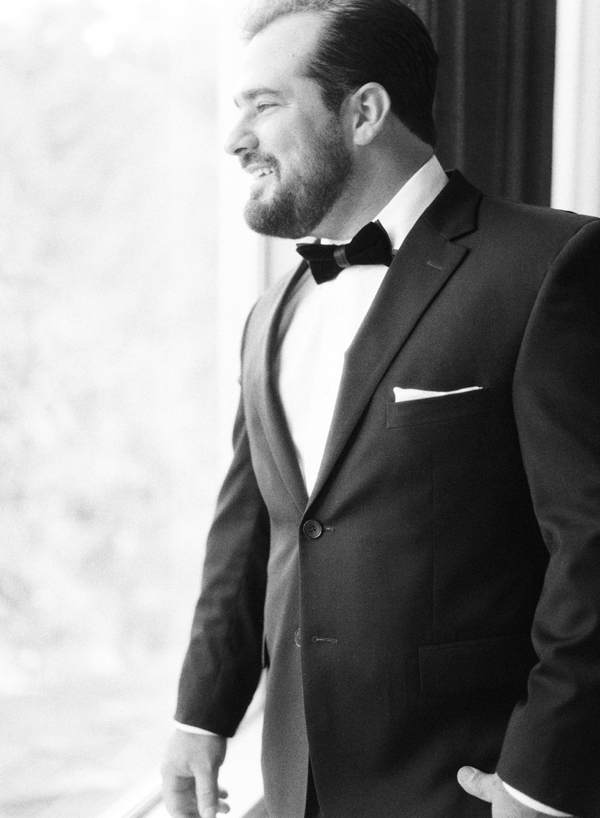 Black and white of a groom smiling out the window.
