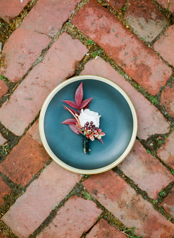 A boutonniere with red leaves and a cream rose sits in a blue terra cotta dish laid on brick at the Swedenborgian Church. 