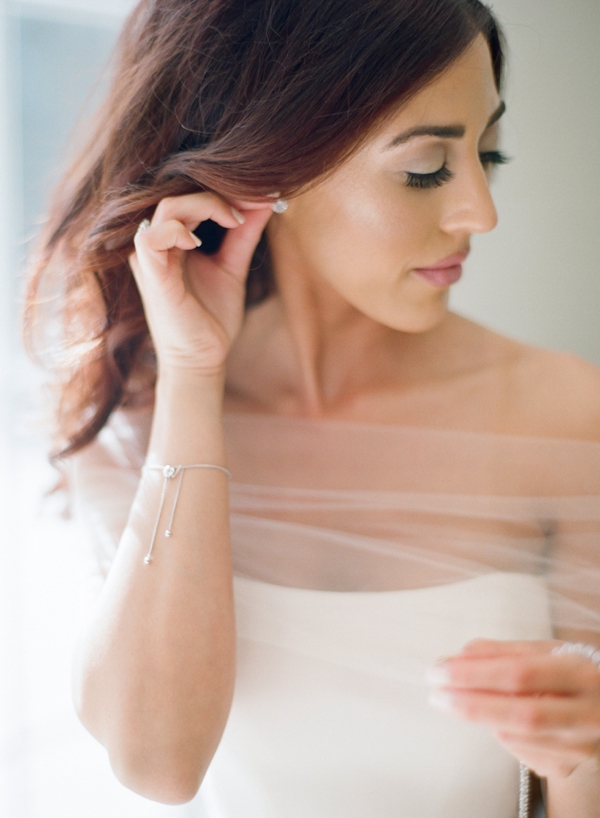 A classic and chic brunette bride adjusts her earrings as she finishes getting dressed. 