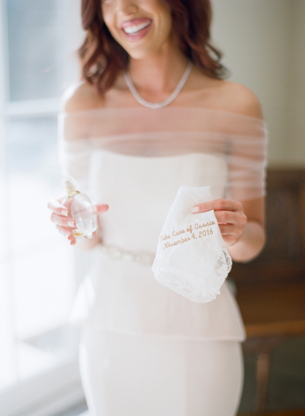 A smiling bride holds a embroidered handkerchief and a bottle of perfume. 