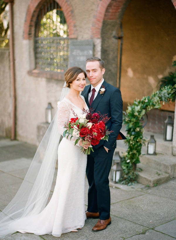 A bride holding a berry colored bouquet and a groom in a navy tux share a portrait in front of the Swedenborgian Church in San Francisco. 