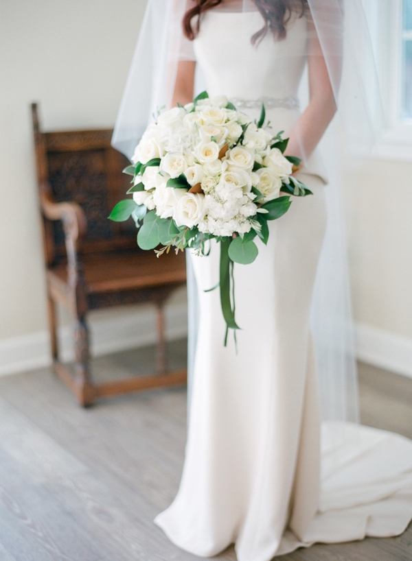 A bride holds a large white rose bouquet.