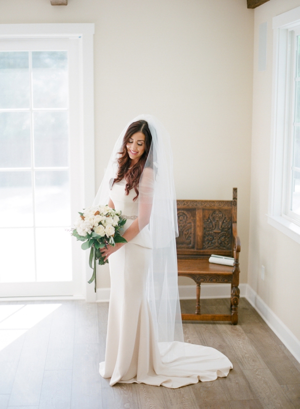 A bride with white rose bouquet stands in her living room in Monterey, CA.