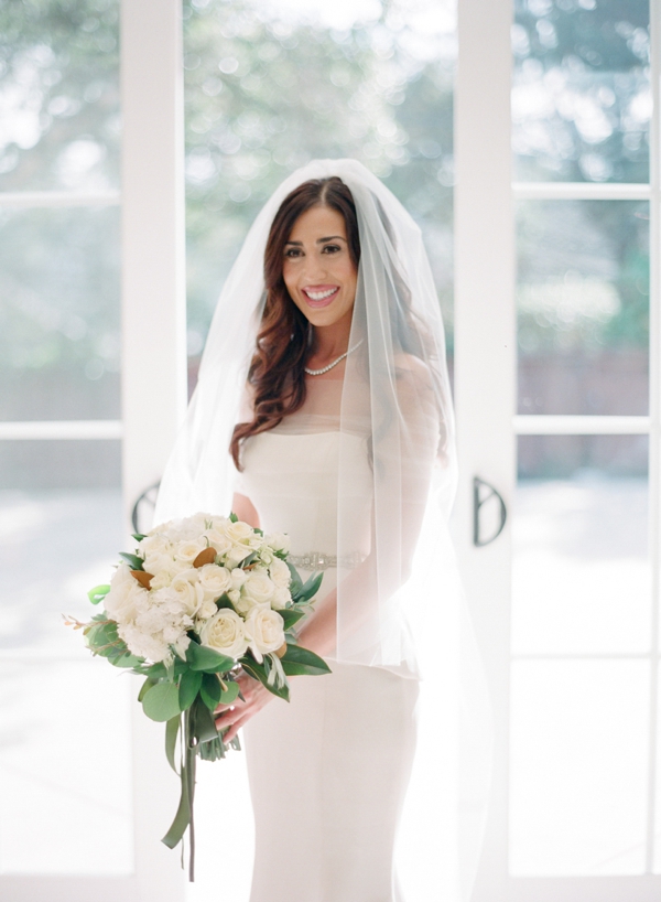 A smiling bride holds a large white rose bouquet. 