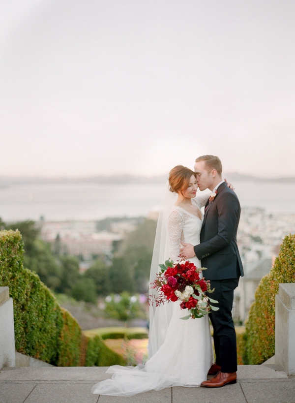 Atop the Lyon Street steps, a bride holding a berry and cream bouquet is kissed on the temple by her groom after their intimate San Francisco City wedding.