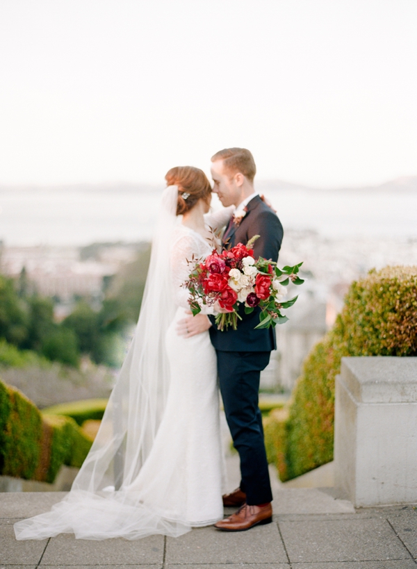 Atop the Lyon Street steps in San Francisco a bride holding a berry and cream bouquet is nuzzled by her husband.