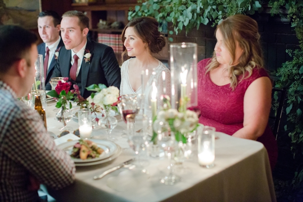 A best man, groom, bride, and maid of honor sit together at a long table during dinner at the Swedenborgian Church in conversation.