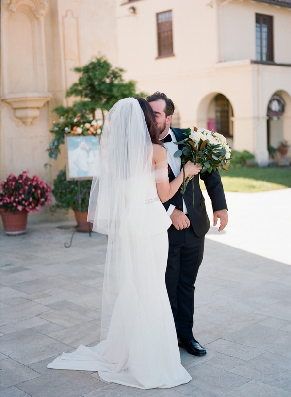 A bride and groom kiss outside of Cathedral of San Carlos Borromeo in Monterey, CA
