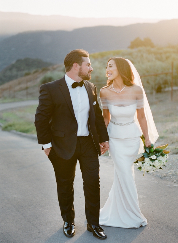 A sunset portrait of a happy bride and groom walking through a road in Carmel Valley at Holman Ranch in California.