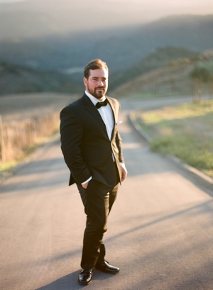 Portrait of a groom in a black tuxedo in a dirt road of Carmel Valley.