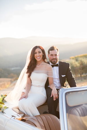 A bride and groom sit together atop a white convertible in Carmel Valley, CA