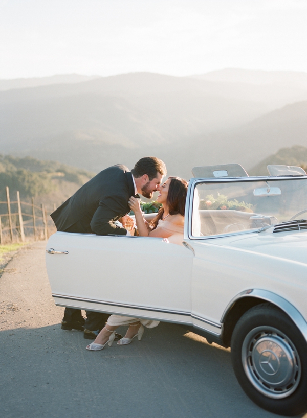 A bride and groom share a kiss as she steps out of the getaway Mercedes convertible car. 