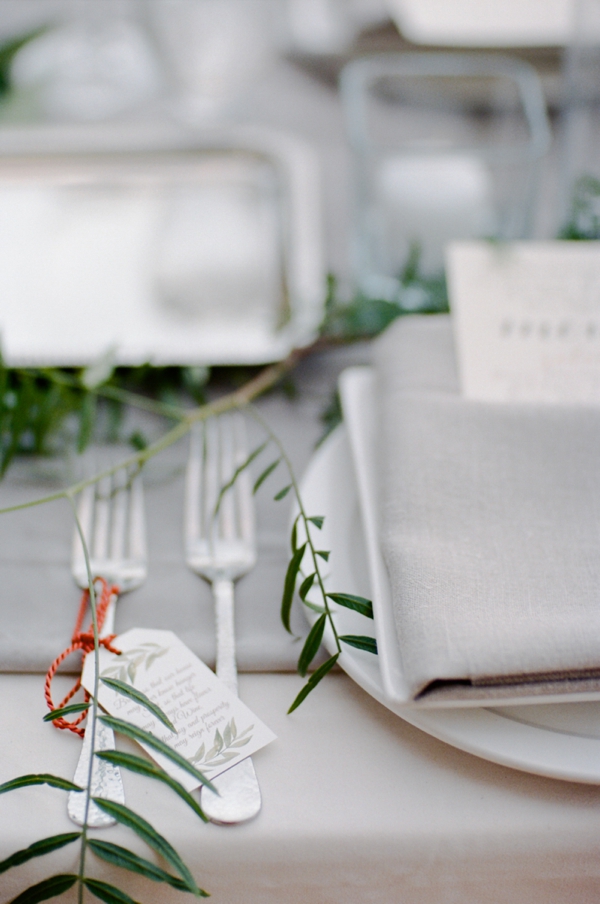 Details of forks at a place setting with grey linens and green ivy.