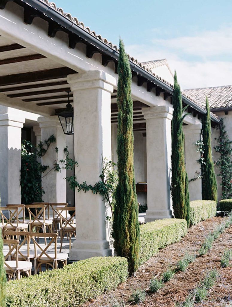 A private residence with white columns and Cypress trees is sits with chairs for guests of a same sex wedding in Sonoma. 