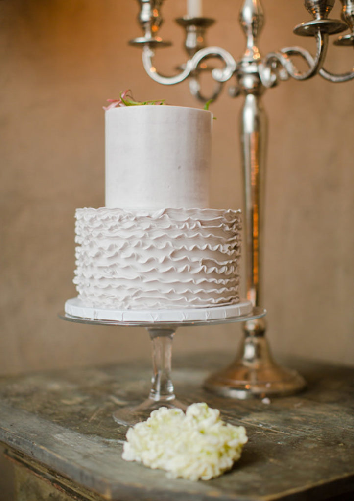 White two tiered wedding cake ion a wood table in a wine cellar.