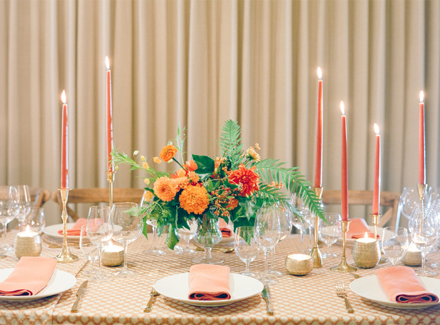 A honey orange carnation flower arrangement sits decorating a dinner table with blood orange tapered candles.