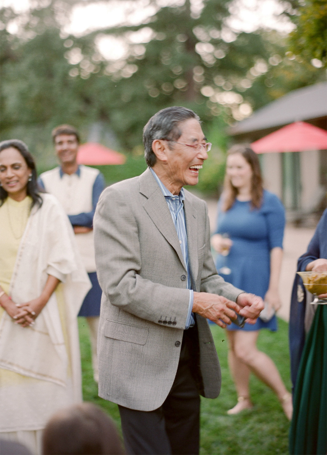 The bride's father laughs as turmeric paste is handed to him to apply to his daughter in an outdoor haldi ceremony in Napa Valley. 