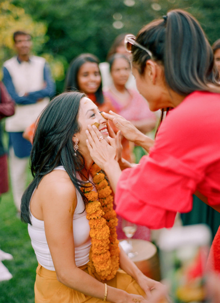 A girl in a red dress applies turmeric paste on the bride during the outdoor haldi ceremony in Napa, California.