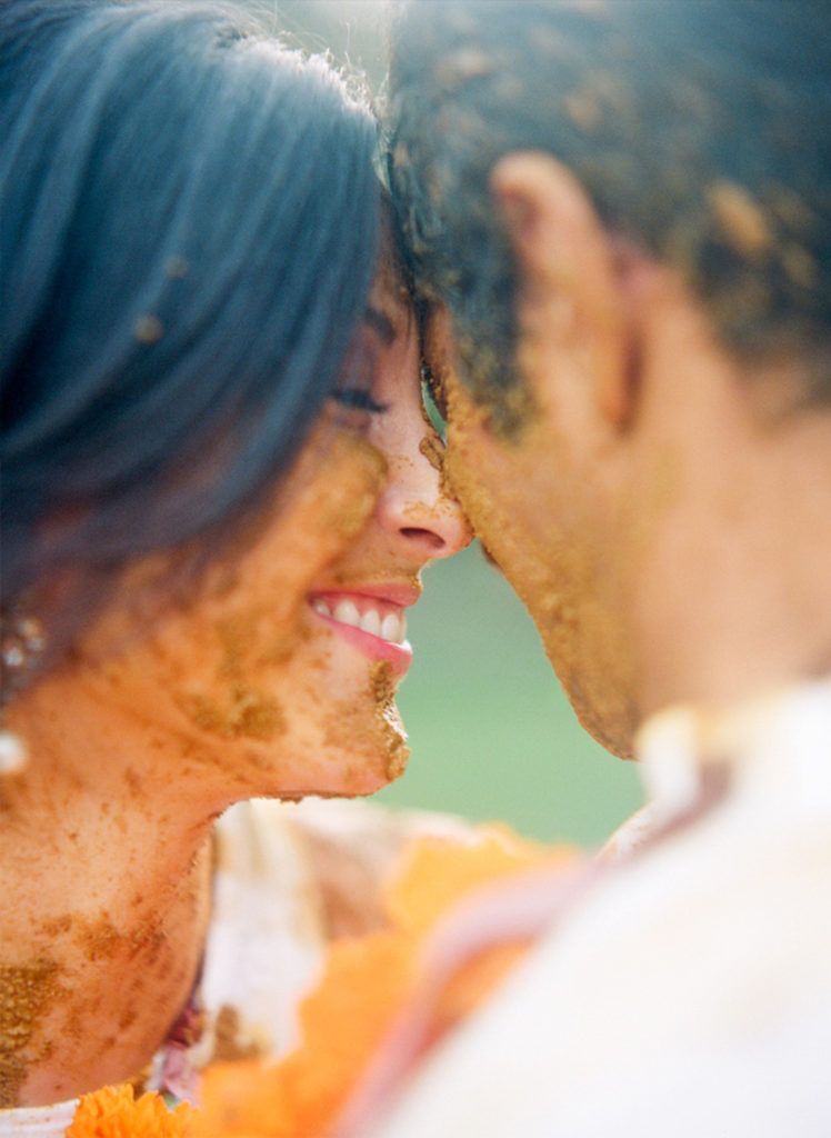 A beautiful backlit photo of Jenna Lam and Alok Patel snuggling while smeared with turmeric paste. 