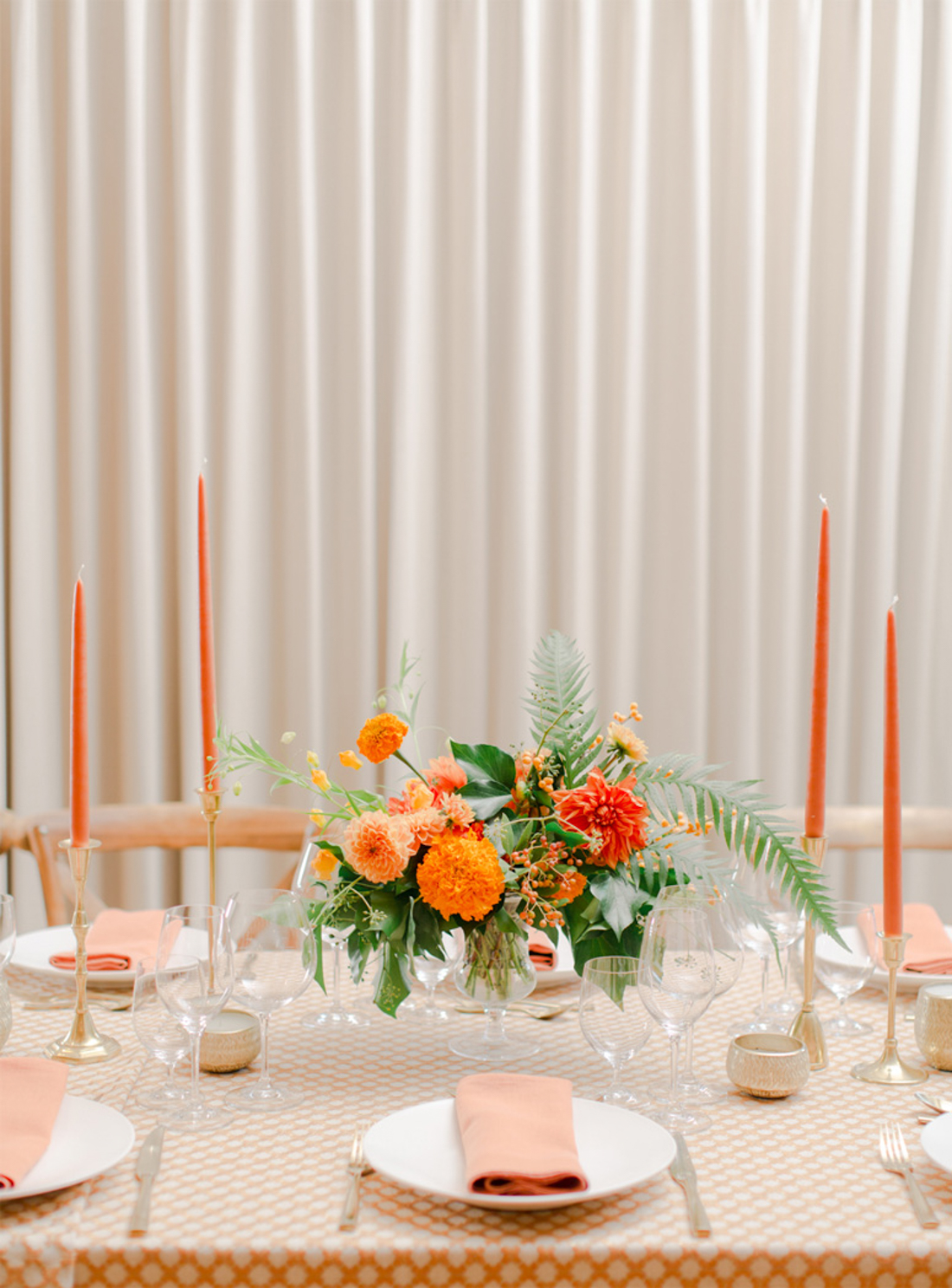 A honey orange flower arrangement sits with orange taper candles decorating a dinner table.