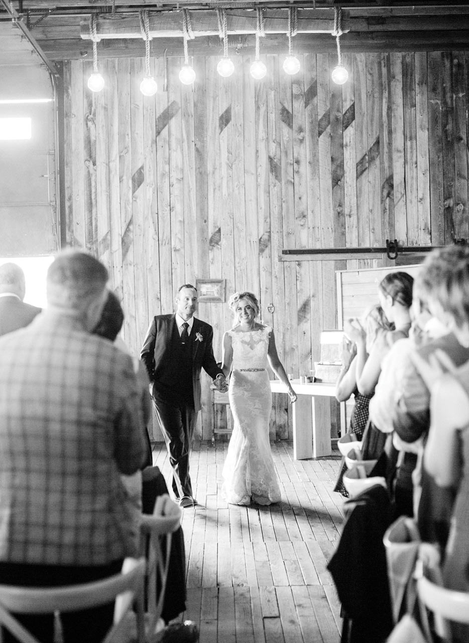 A bride and groom enter their wedding reception filled with cheers and applause from guests at High West Distillery.
