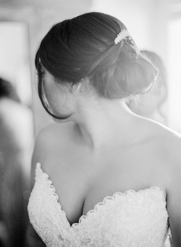 A bride with her hair up in a bun and strapless dress looking into mirror after getting dressed 