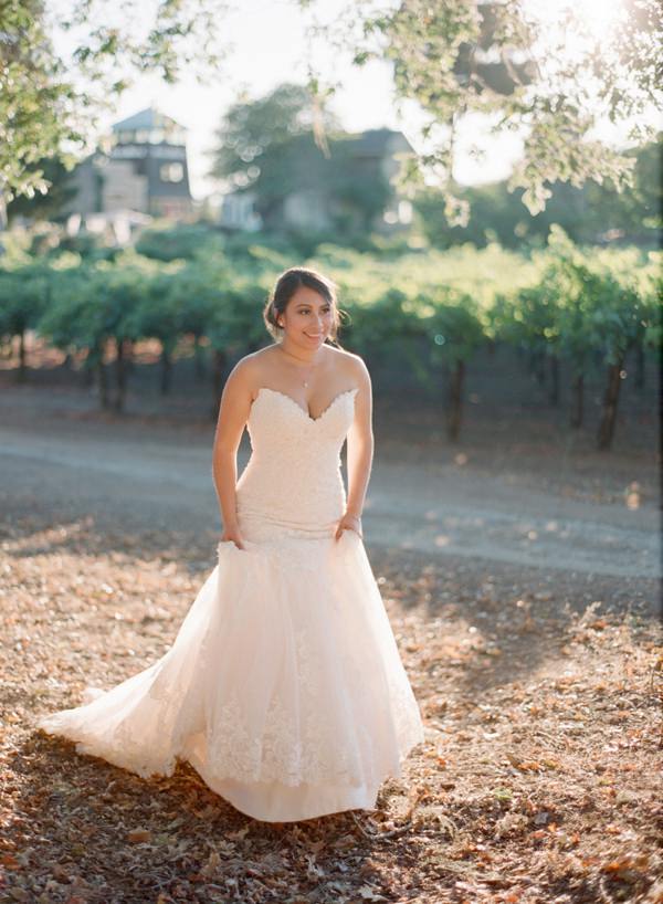 Bride holding dress as she walks near a vineyard with the sun setting