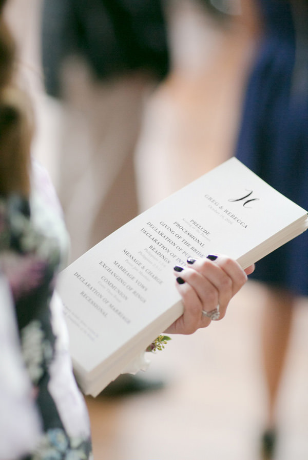 A girl with blue fingernail polish holds a stack of long white and printed wedding programs.