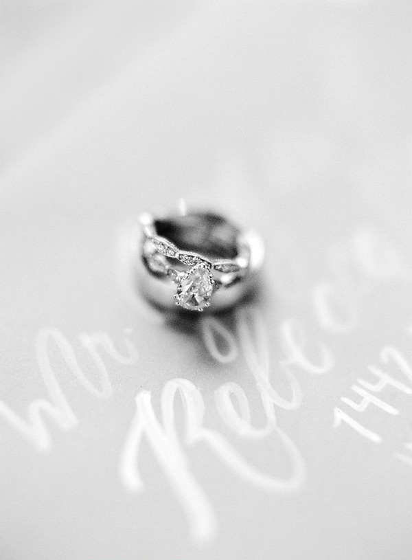 A black and white close up of wedding rings and engagement ring sitting on top of handwritten calligraphy names