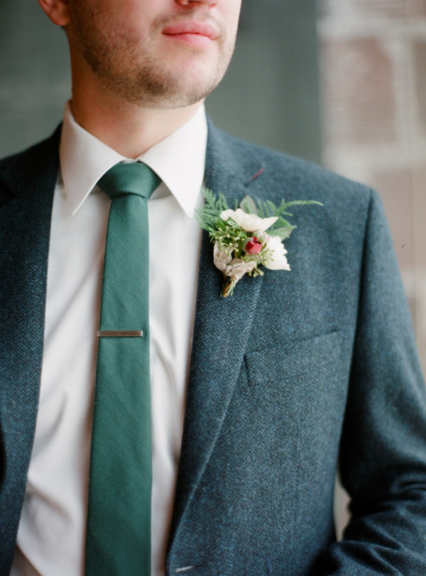 Closeup of the white and green boutonniere pinned to a blue tweed suit jacket with a forest green tie