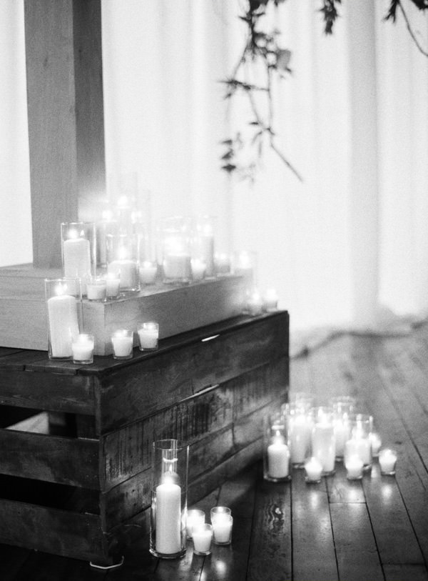 Lots of candles in glasses strewn on the floor and on the base of a large wooden cross made for a wedding ceremony. 