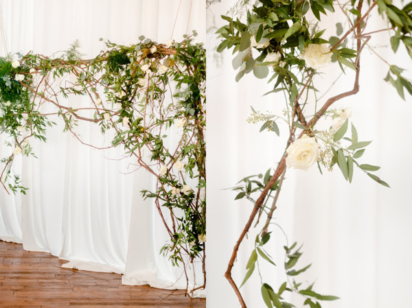 Rose and olive branch wedding ceremony installation in front of white drapes inside a venue wth wood floors