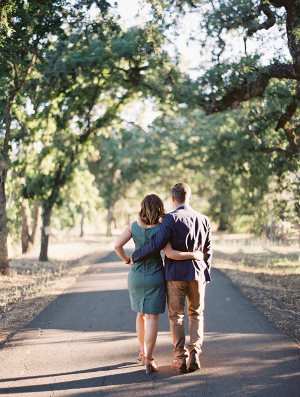 Couple walk away together down a road with their arms around each other's waist.