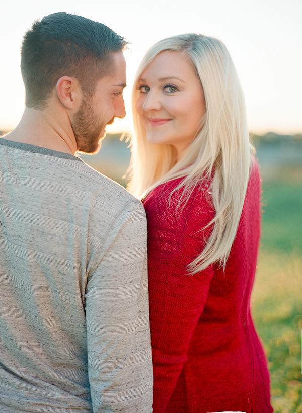 Blonde haired girl in a red sweater turns to the camera beside her husband